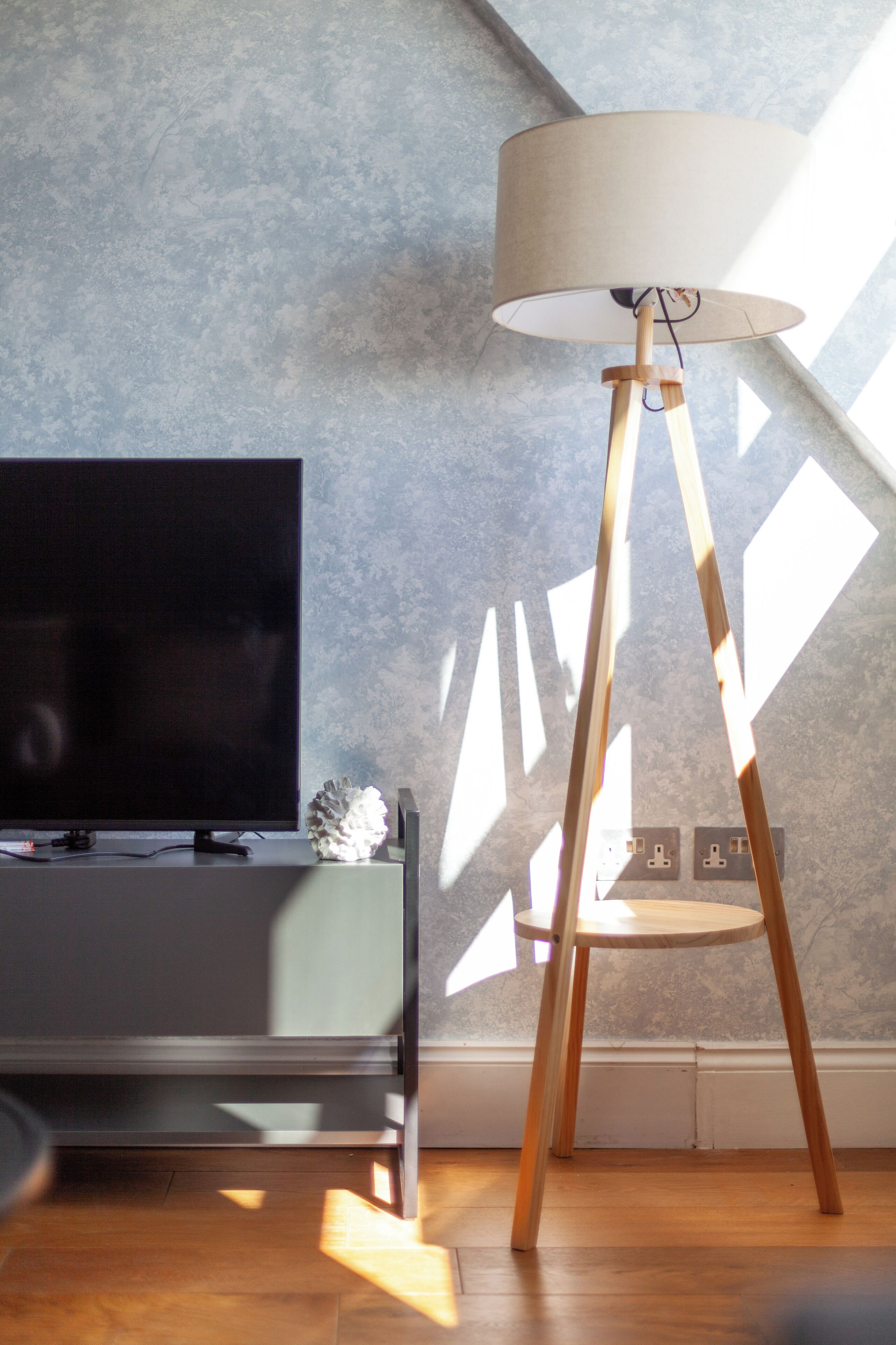 Een moderne woonkamer met een flatscreen televisie, een houten vloerlamp en een decoratief object op een console tafel.