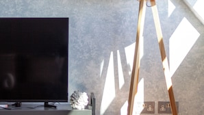A modern living room with a flat-screen TV, a wooden floor lamp, and a decorative piece on a console table. - The South Hampstead Collection (London)