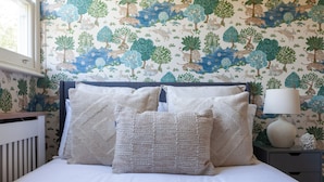 A bedroom with a bed, pillows, a nightstand, a lamp, and a window. - The South Hampstead Collection (London)