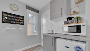 A modern kitchen with a built-in microwave, a refrigerator, and a flat-screen TV mounted on the wall. - Captivating 1-bed Studio in West Drayton (West Drayton)