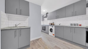 A modern kitchen with grey cabinets, a built-in oven, and a washing machine. - Captivating 1-bed Studio in West Drayton (West Drayton)