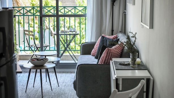 Een knus ingerichte kamer met een bank, een klein tafeltje, een fruitschaal en uitzicht op een balkon met een tafel en stoelen.