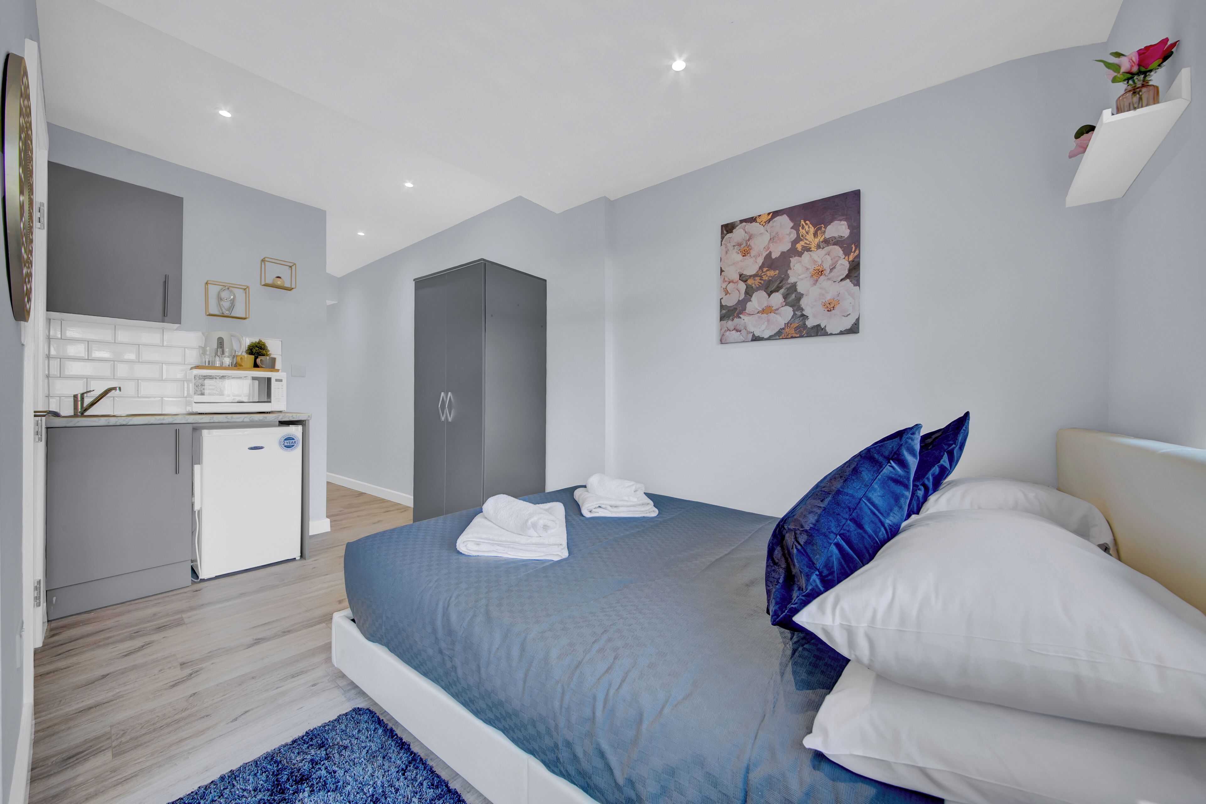 A modern bedroom with a bed, pillows, and a small kitchenette.