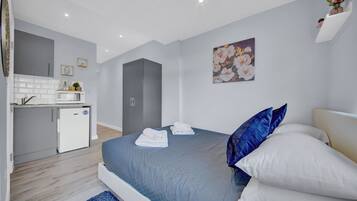 A modern bedroom with a bed, pillows, and a small kitchenette.