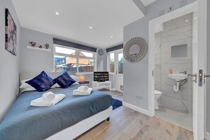A modern bedroom with a large bed, a bedside table with a TV, a bathroom with a shower, and a view of the outside. - Charming Serviced Studio West Drayton London UB7 (West Drayton)