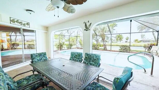 Un'area pranzo all'aperto coperta, con tavolo e sedie, ampie finestre e una ventola a soffitto.