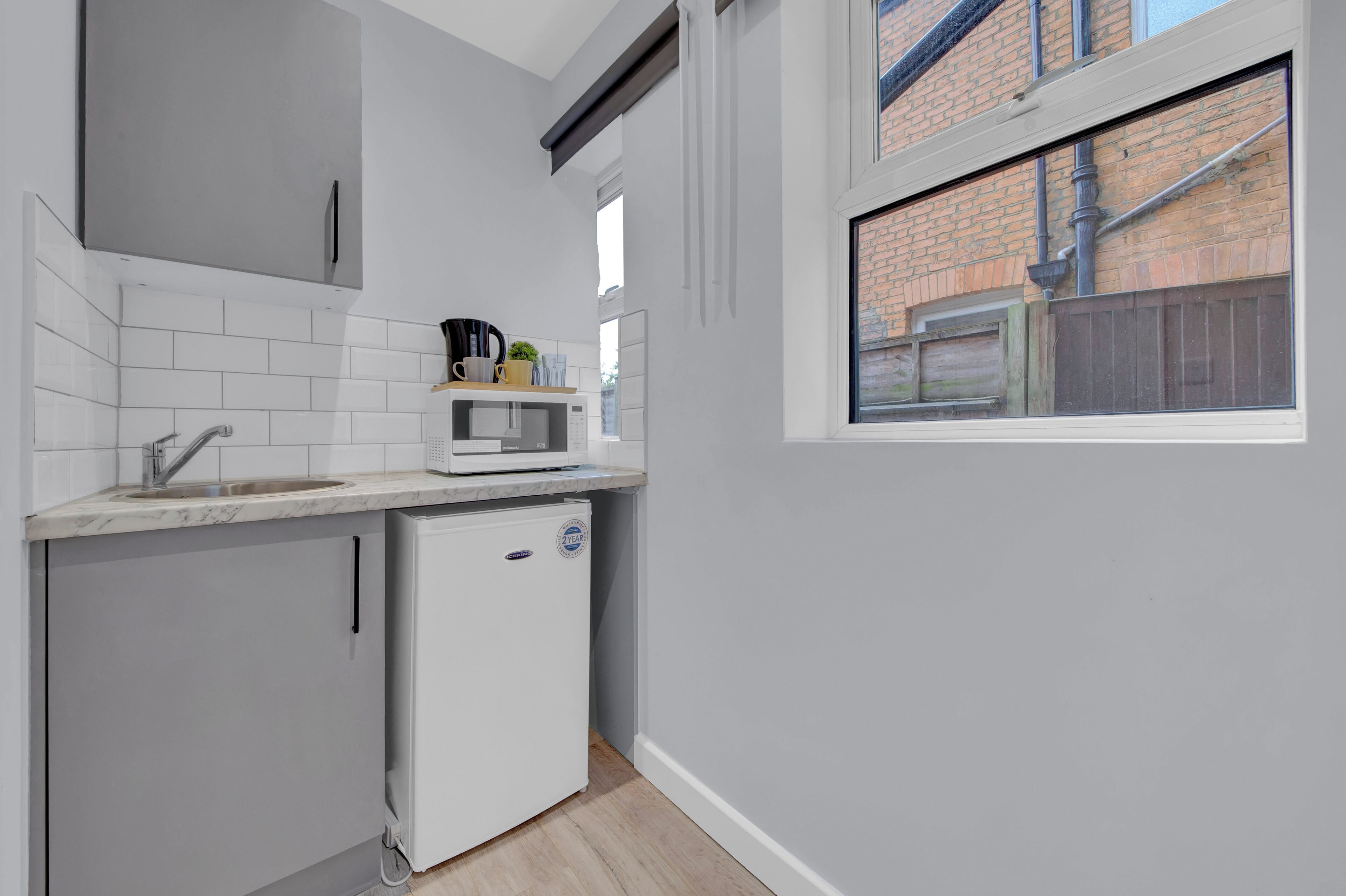A compact kitchen with a built-in microwave, a small refrigerator, and a window overlooking a brick building.