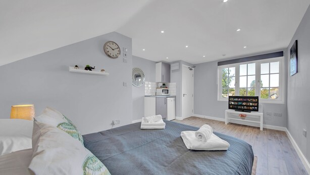 Un dormitorio moderno con cama, televisión, kitchenette pequeña y ventana grande.