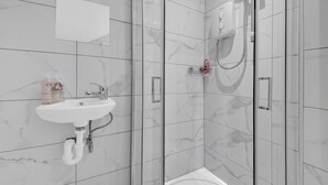 Un baño moderno con ducha envuelta en vidrio, un lavabo blanco y azulejos de mármol.
