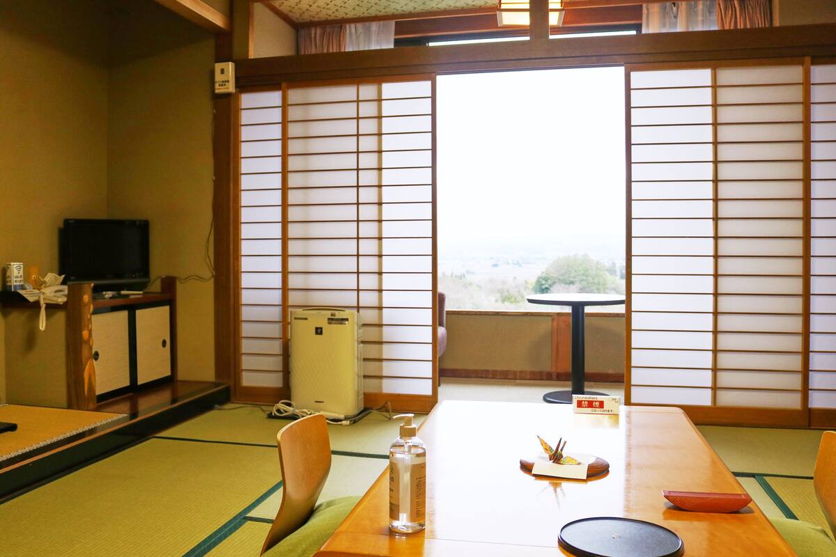 Une pièce de style japonais traditionnel, avec un sol recouvert de tatamis, une petite table basse avec un coussin, un téléviseur et un radiateur.