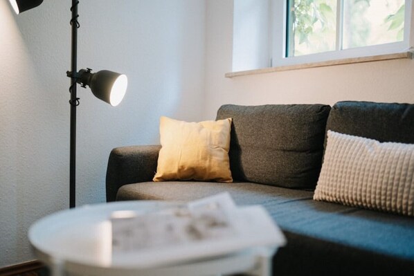 Ett vardagsrum med en soffa, två kuddar, en golvlampa och ett litet bord med en tidning på.