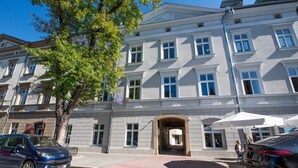 A multi-story building with a central entrance, large windows, and a tree in front. - City Lights Mostowa (Kraków)