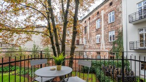 A courtyard with a round table and chairs, surrounded by a black metal fence. - City Lights Mostowa (Kraków)