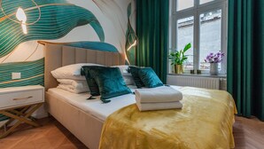 A modern bedroom with a large bed, a nightstand, a bedside table, and a window with curtains. - City Lights Mostowa (Kraków)