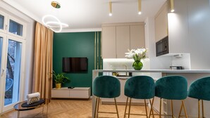 A modern kitchen with a white countertop, teal bar stools, and a green accent wall. - City Lights Mostowa (Kraków)