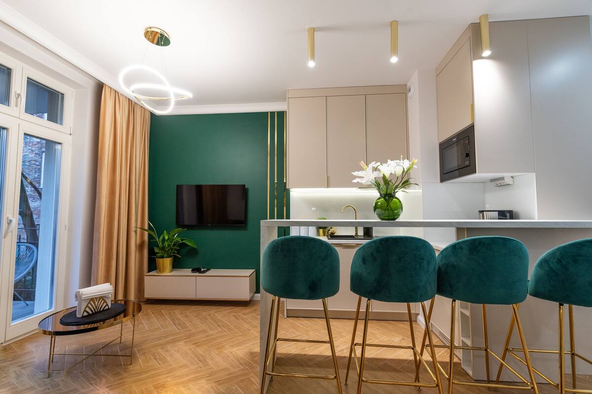 A modern kitchen with a white countertop, teal bar stools, and a green accent wall.