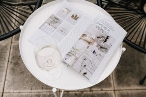 Une table blanche sur laquelle se trouvent un verre de vin blanc, un magazine et une carte.