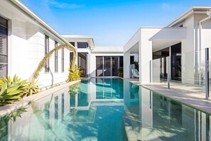 A modern house with a swimming pool, large windows, and a clear sky.