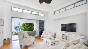 A modern living room with a large TV, white furniture, and a balcony with plants. - Hampton Beach House on the Waterfront (Buddina)