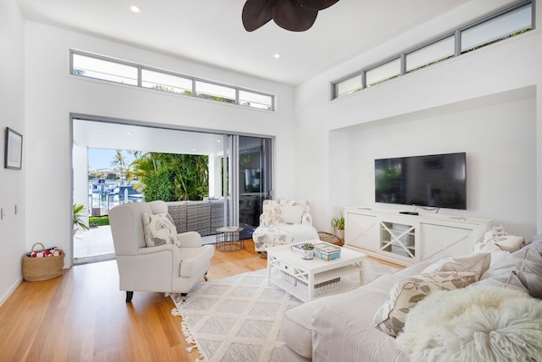 A modern living room with a large TV, white furniture, and a balcony with plants.