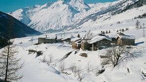 Un pueblo cubierto de nieve con edificios de piedra tradicionales, una iglesia y montañas al fondo.