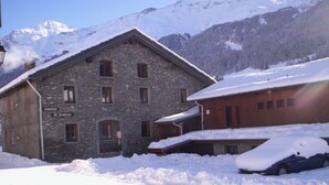 Un edificio de piedra con un cartel que dice "Auberge de Jeunesse" en un paisaje nevado con montañas al fondo.