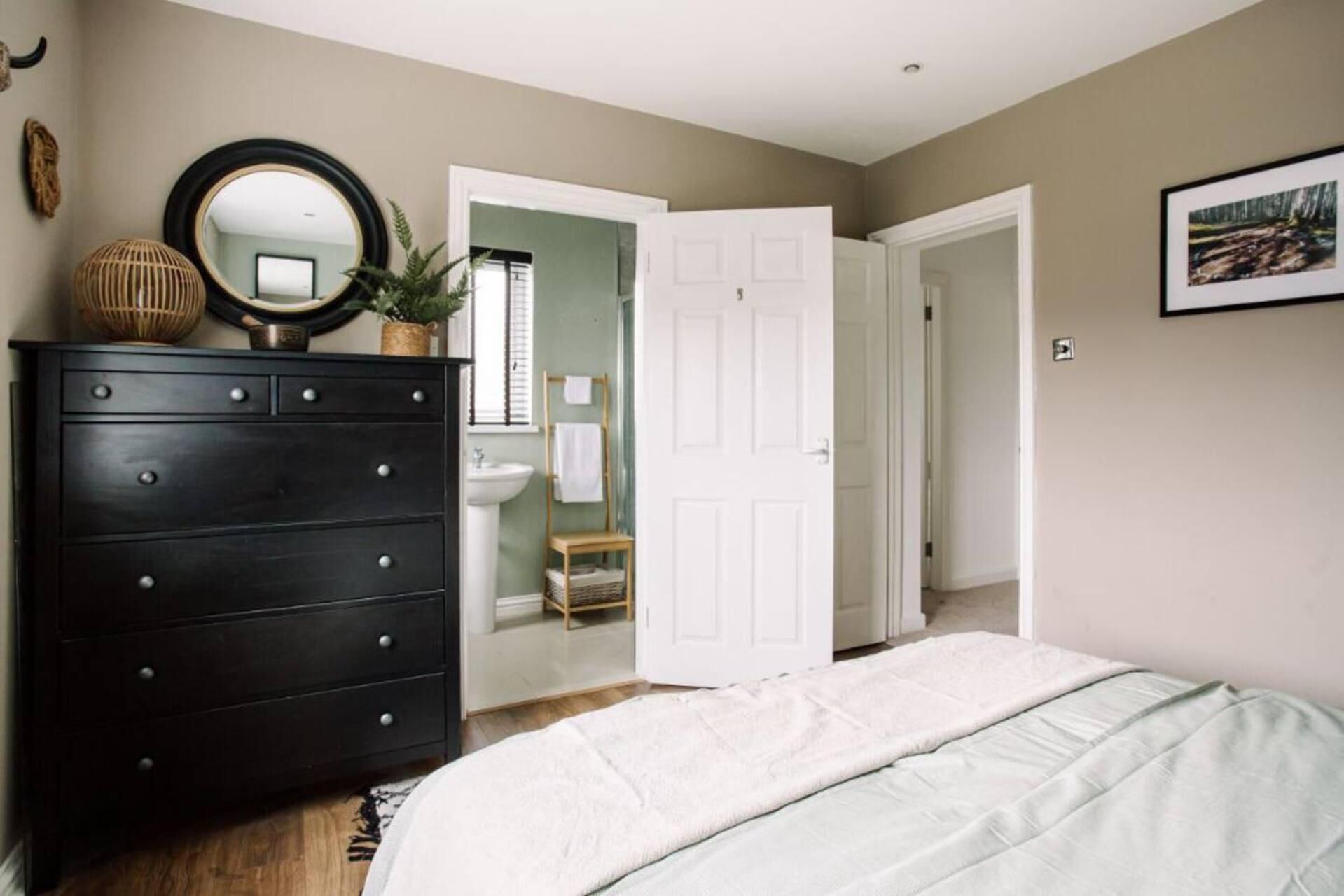 A bedroom with a bed, a dresser, a mirror, a door leading to a bathroom, and a framed picture on the wall.