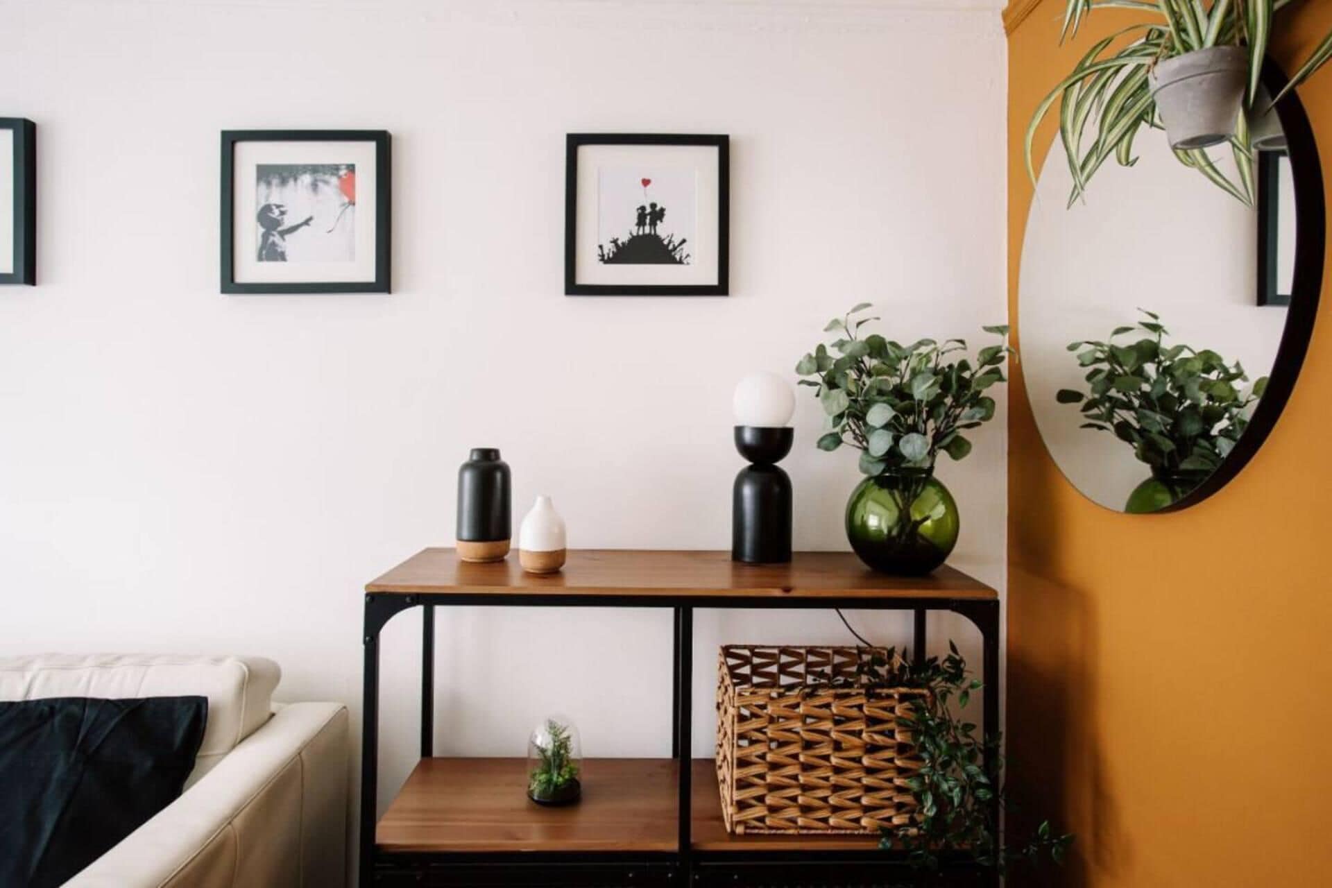 Een woonkamer met een bank, een salontafel met decoratieve voorwerpen, ingelijste foto’s aan de muur, en een spiegel die een plant reflecteert.