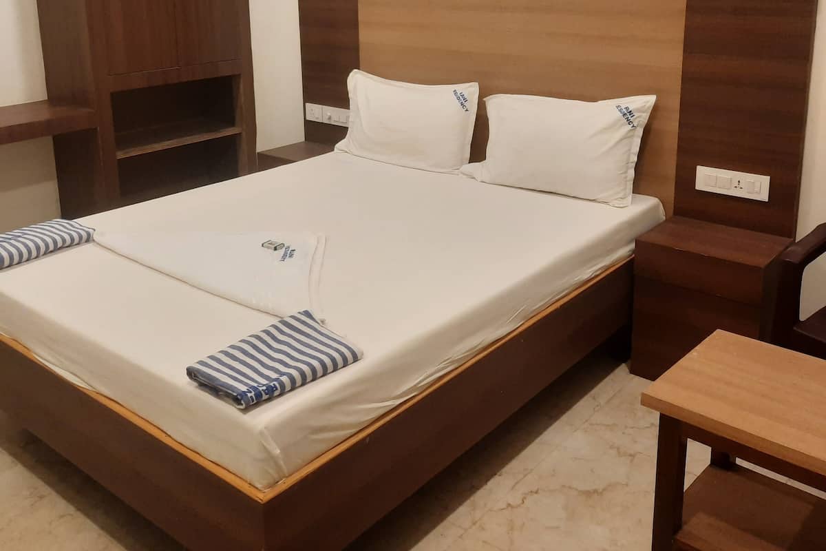 A single bed with white bedding, two pillows, and a striped pillow. There is a wooden nightstand with a lamp and a wooden wardrobe with two doors.