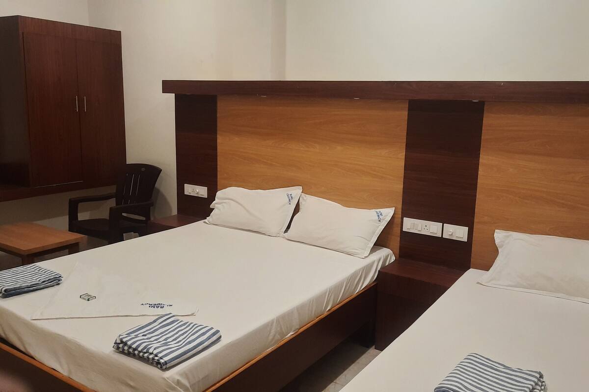 A hotel room with a large bed, a smaller bed, a desk, a chair, and a wardrobe.