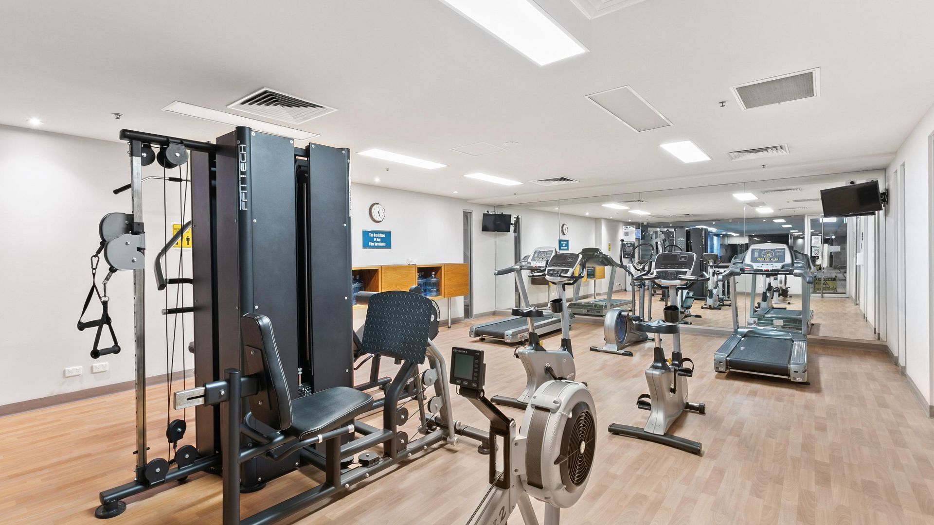 A gym with various exercise equipment, a clock, and a water dispenser.