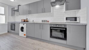A modern kitchen with grey cabinets, a built-in oven, a microwave, and a washing machine.