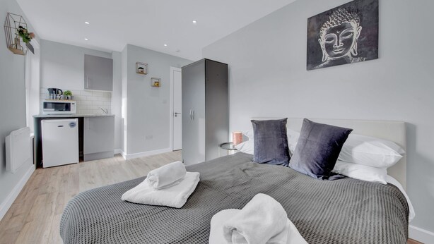 A modern bedroom with a large bed, a small kitchenette, and a minimalist design.