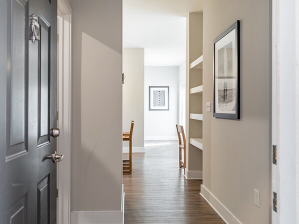 A hallway with a wooden door, a framed picture on the wall, and a dining area with chairs and a table. - Vintage Amelia Island Apartments (Fernandina Beach)