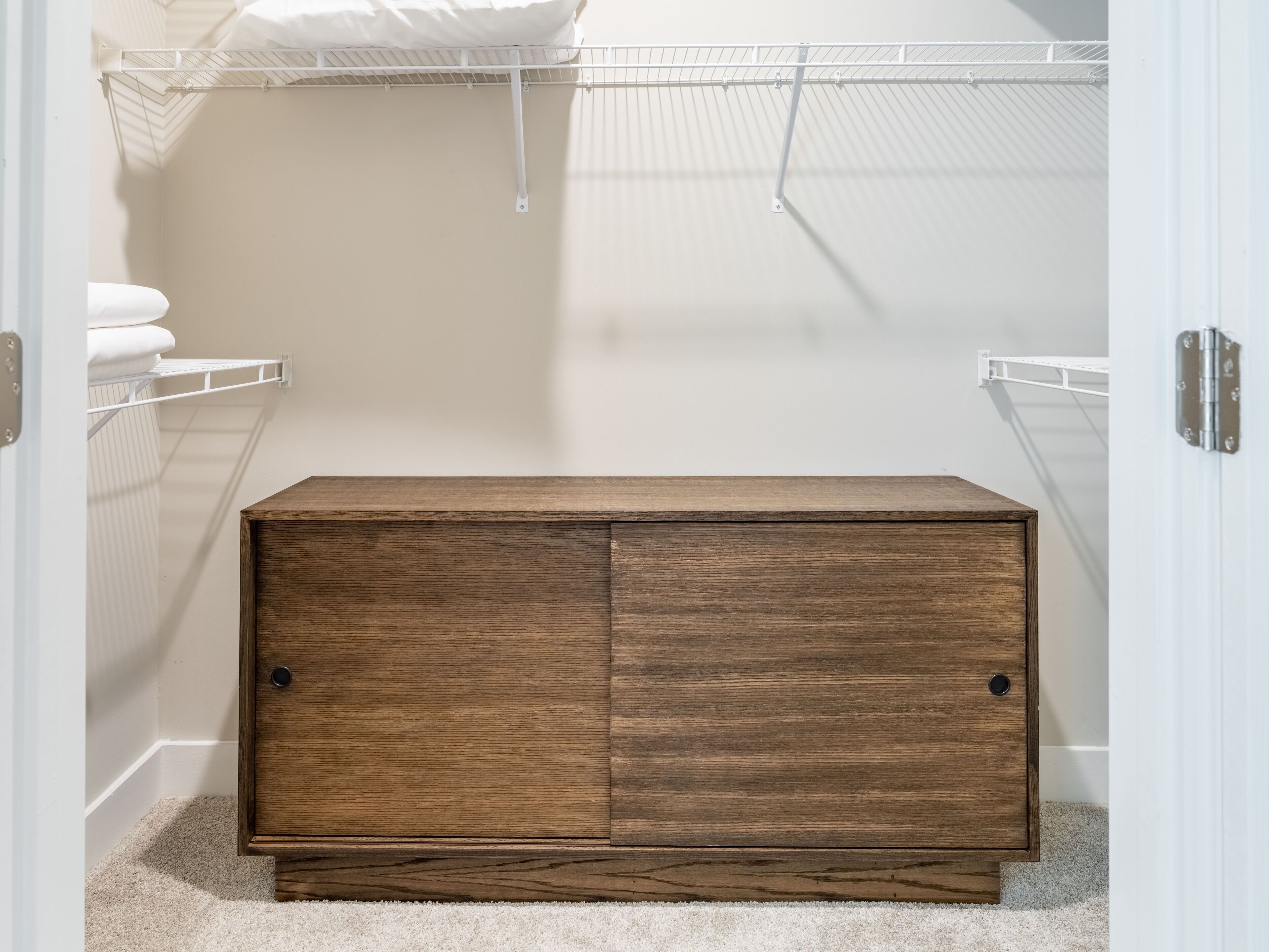 A walk-in closet with a wooden chest of drawers, metal shelving, and a white door.