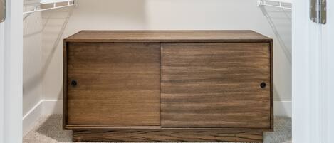 A walk-in closet with a wooden chest of drawers, metal shelving, and a white door.