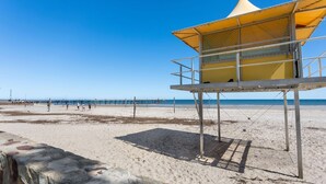 A beach with a lifeguard tower, clear blue sky, and a pier in the background.
