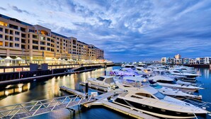 A marina with multiple yachts docked, a waterfront hotel with balconies, and a clear sky. - Belle Escapes - Sunny Siesta at Glenelg (Glenelg)