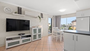 A modern apartment with a flat-screen TV, a dining area, and a kitchen. - Belle Escapes - Sunny Siesta at Glenelg (Glenelg)