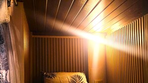 Een kamer met een schuine kap, een bed met een kussen met een patroon, en een wand met verticale jaloezieën.