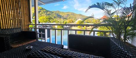 A balcony with wicker furniture, a view of a lake, and a mountain in the background.