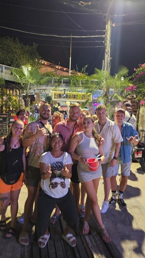A group of people posing for a photo in an outdoor setting with a sign that reads "CADEUM HOSTEL".
