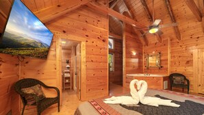 A wooden cabin interior with a bed, a television, a ceiling fan, and a bathroom.