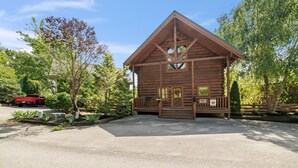 Una cabana de fusta amb un porxo, envoltada d'arbres i un camí d'accés asfaltat.