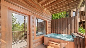 A wooden cabin with a hot tub, wooden deck, and large windows.
