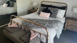 A neatly arranged bedroom with a bed, a bedside table, a lamp, and a mirror.