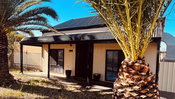 A house with a covered porch, a palm tree, and a large window.