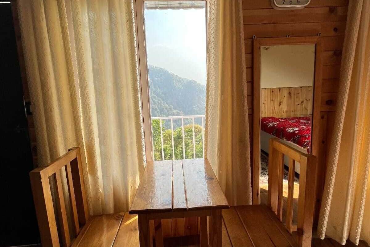 Een houten chalet met een tafel en stoelen, een raam met gordijnen en een klok aan de muur.