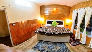 Een slaapkamer met een gebogen houten wand, een bed met een beddeken met dessin, en een raam met gordijnen.
