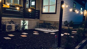 A single-story house with a front porch, a small garden area with stepping stones, and string lights. - ATL: 6BR Triplex—Chic, Boho,Retro Vibes |Sleeps 16 (Atlanta)